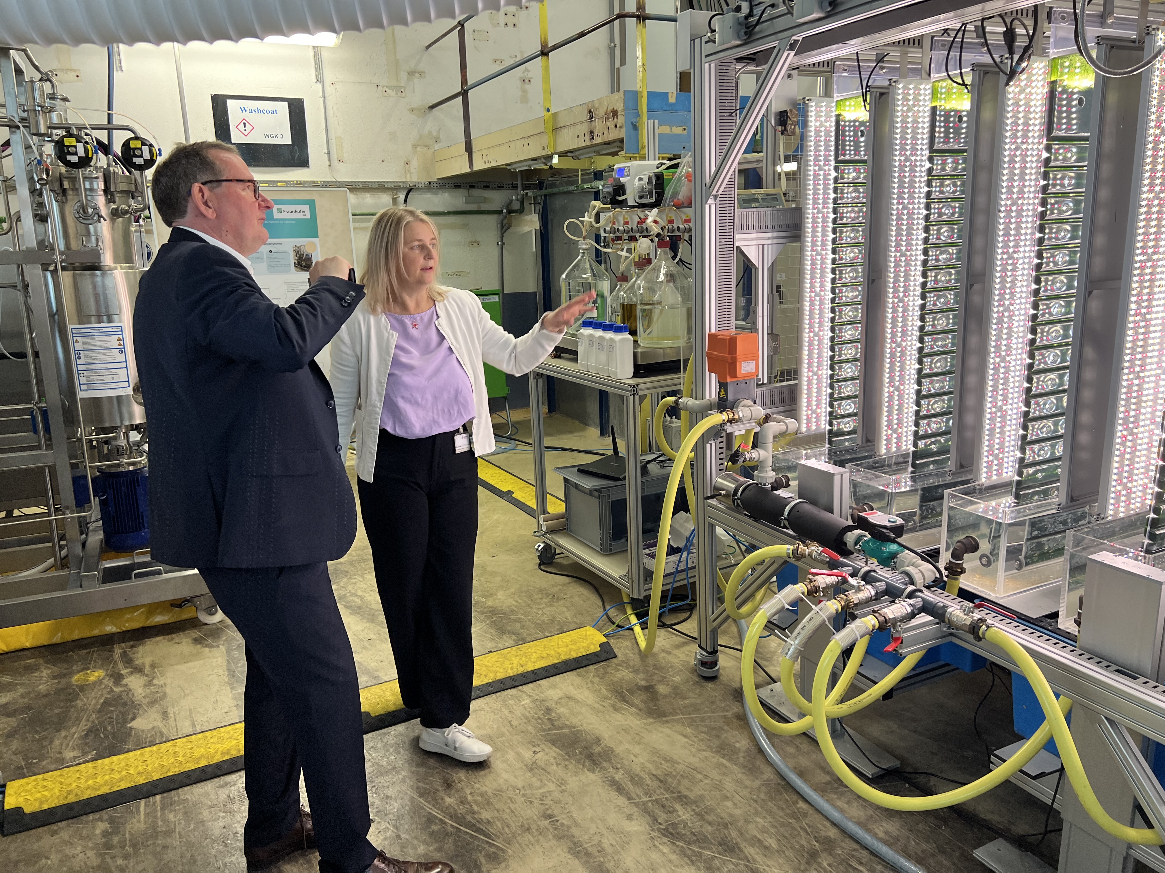 Standortleiter Hermann Becker (Evonik) im Gepräch mit Projektkoordinatorin Dr.-Ing. Ursula Schließmann (Fraunhofer IGB) vor der Bioraffinerie, die aus gekoppelten biotechnologischen Verfahren mit Purpurbakterien in geschlossenen Bioreaktoren (links) und Mikroalgen in einem kompakten Photobioreaktor (rechts) besteht.